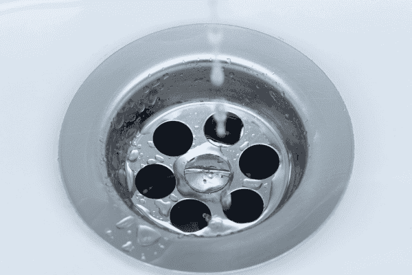Water flowing into a circular metal sink drain with multiple holes, surrounded by a clean white surface.