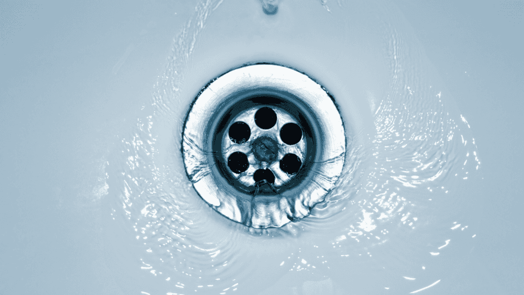 Water flowing down a stainless steel sink drain, creating a swirling pattern around the edges.
